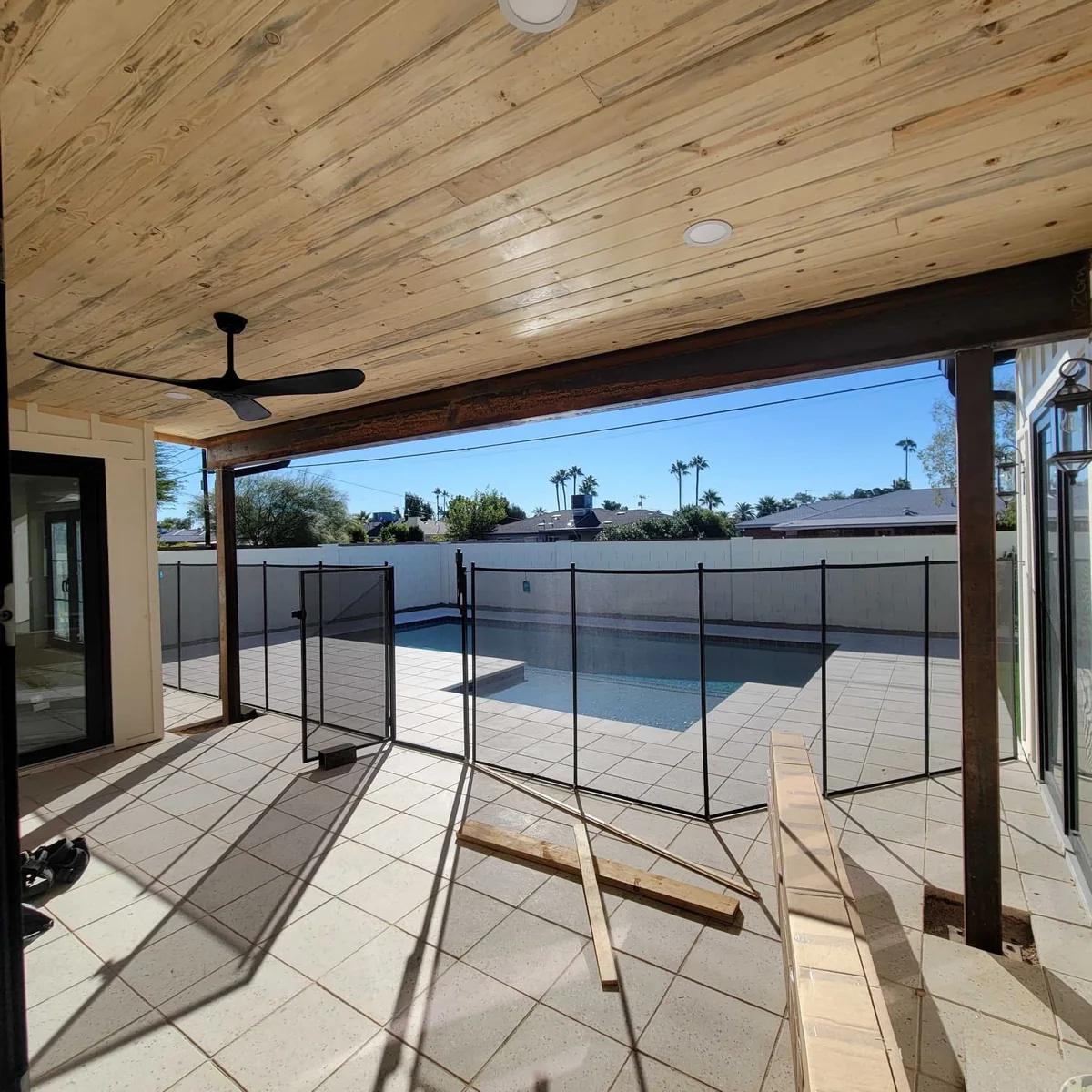 Tile-finished poolside patio with a safety fence, wood ceiling, and ceiling fan