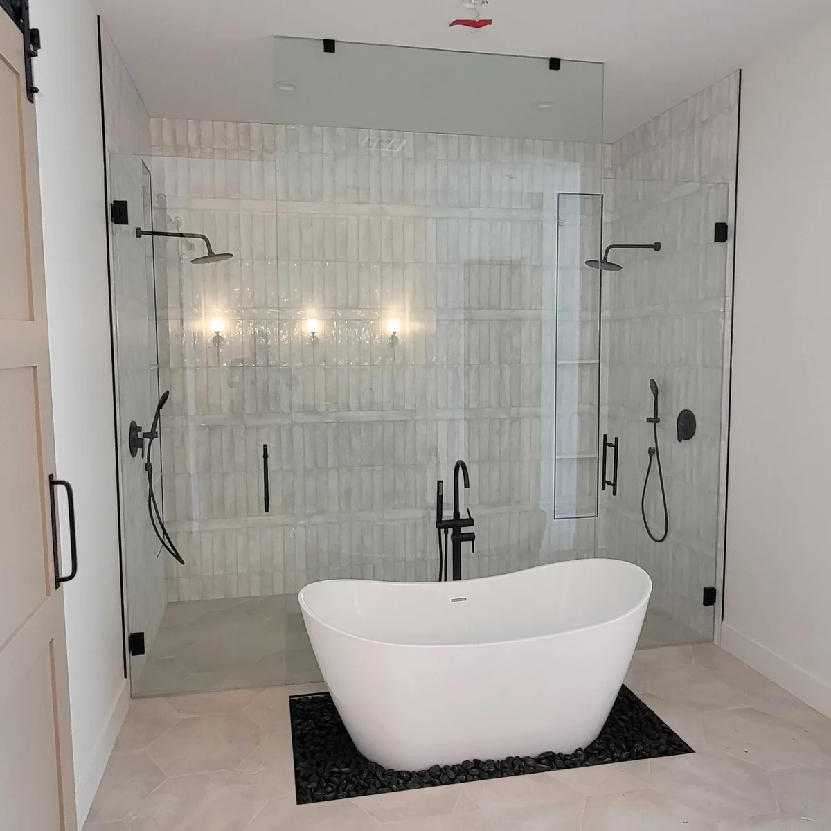 Freestanding bathtub in front of a glass-enclosed shower with white tile and black fixtures