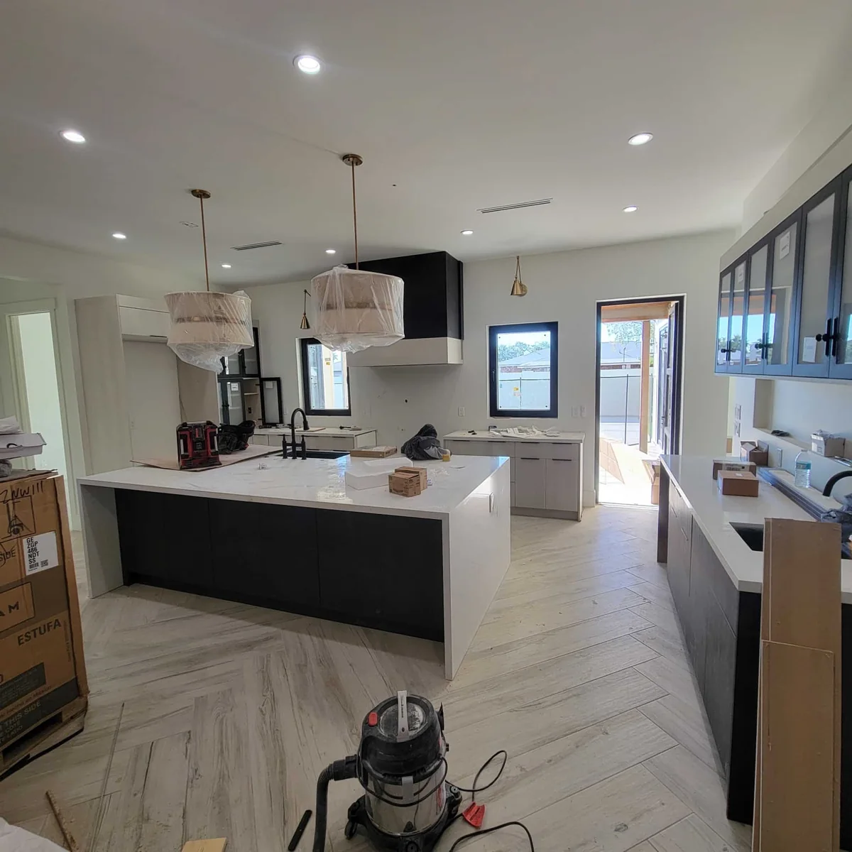 Kitchen remodeling in progress with a large island, dark base cabinets, white counters, and pendant lights